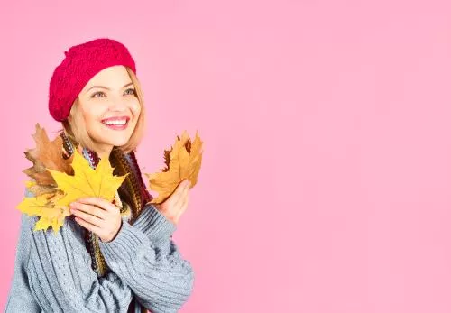 تصویر زمینه دختر درحال لبخند زدن با برگ های افرا پاییزی نارنجی با کیفیت فوق العاده با زمینه صورتی 22019